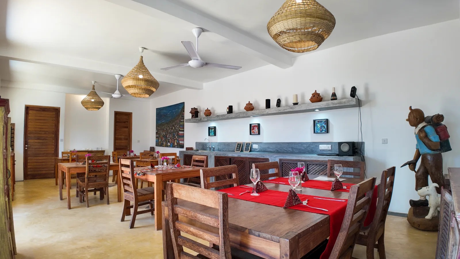 Khole Villa dining room with timber furniture, woven lights, art, and red table settings
