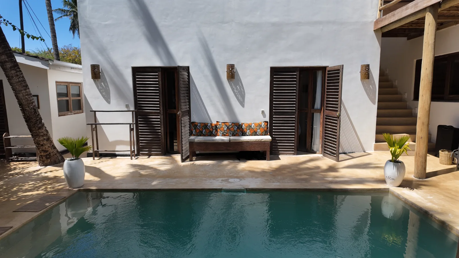 Khole Villa courtyard pool framed by white walls, timber shutters, and a palm tree