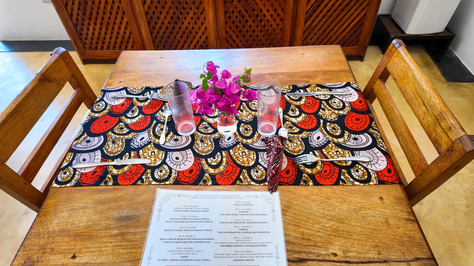 Khole Villa dining table with patterned fabric, glassware, and pink flowers